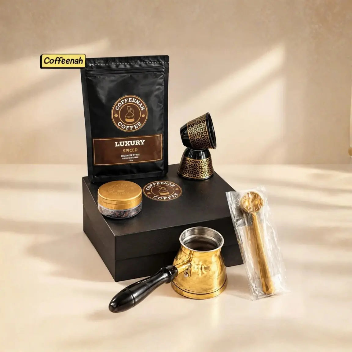 Coffeenah Coffee Luxury Spice gift set featuring a black coffee bag, brass cezve, wooden spoon, and accessories arranged on a black gift box against a warm beige background.