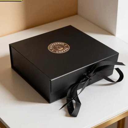A black rectangular gift box with a black ribbon bow, featuring a circular gold logo that reads 'COOSENAR COFFEE' on the top lid, set on a white surface.
