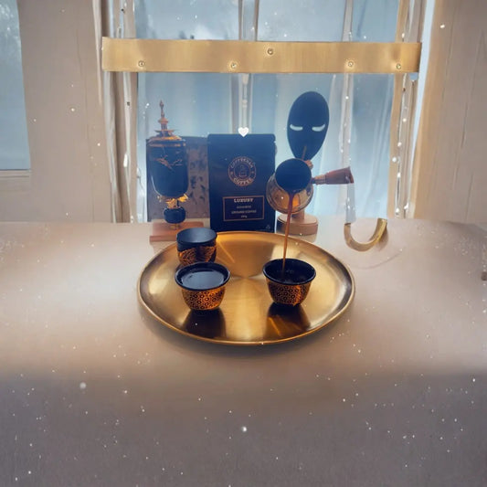 A luxury tea presentation set on a round gold tray, featuring a gold teapot pouring tea into small dark blue and gold patterned cups, with a dark blue box labeled 'LUXURY' and decorative masks in the background.